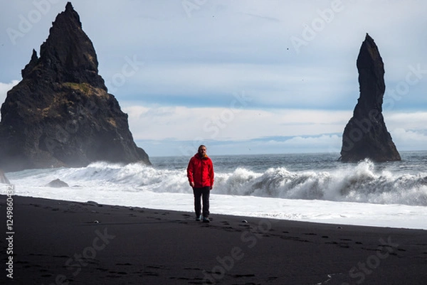 Obraz A person walking along a stunning black sandy beach Reynisfjara and rocky terrain in VIK Myrdal in Golden Circle area in Iceland with Atlantic Ocean waves crashing and volcanic rock formations