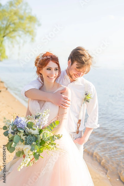 Obraz the happy couple groom and bride with wedding bouquet are on the beach
