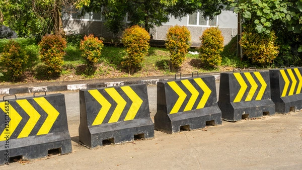 Fototapeta Concrete Barriers with Yellow Arrows on Urban Road Near Greenery
