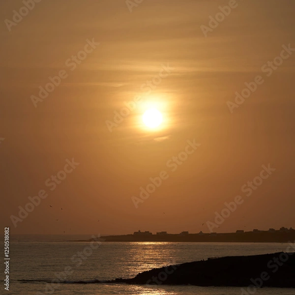 Fototapeta Sunset over the coast in France. Village silhouette by the sea in Brittany. Landscape ideal as background for postcard.