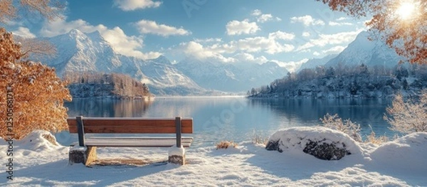 Fototapeta Scenic winter lake landscape with park bench under bright blue sky and mountains creating an inspirational and serene atmosphere