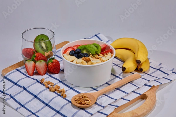 Fototapeta A vibrant and healthy smoothie bowl topped with fresh strawberries, blueberries, kiwi, banana slices, almonds, and pistachio. Placed on a paper cup.