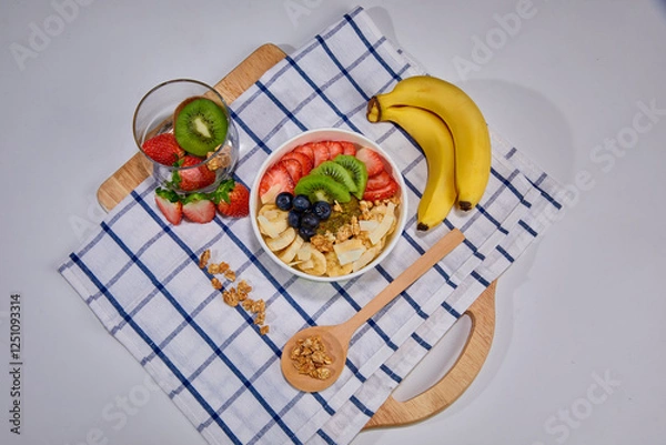 Fototapeta A vibrant and healthy smoothie bowl topped with fresh strawberries, blueberries, kiwi, banana slices, almonds, and pistachio. Placed on a paper cup.