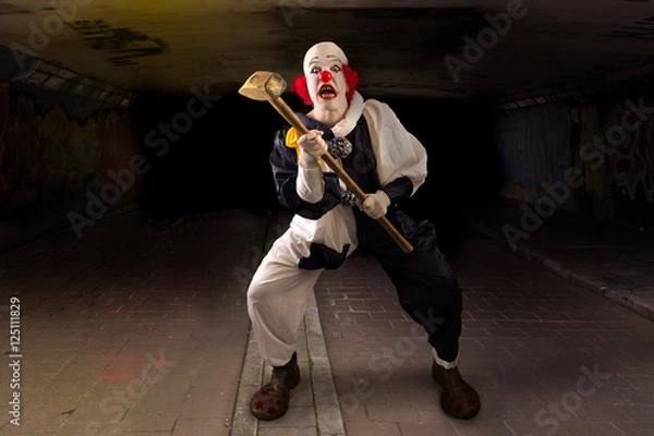 Obraz scary clown with a hammer standing in a tunnel