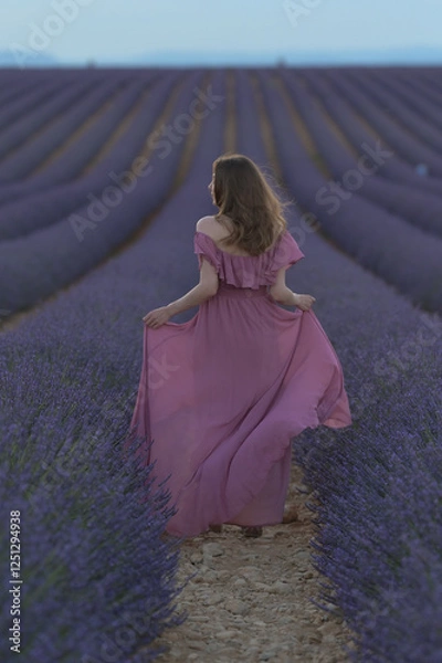 Obraz Ein Mädchen mit offenen Haaren in einem wehenden Kleid in einem Lavendelfeld am Abend.
