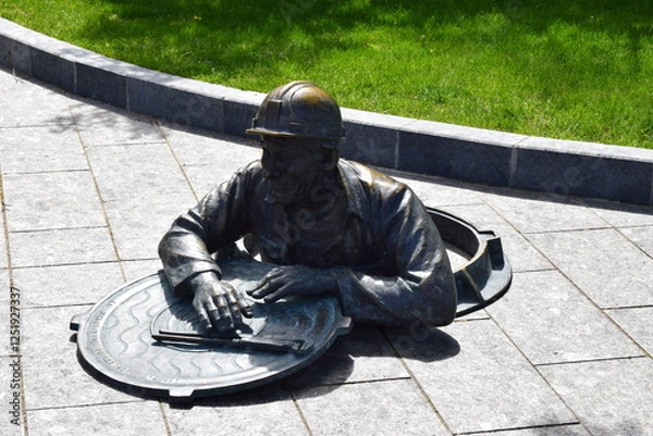 Fototapeta A bronze sculpture of a worker climbing out of a manhole.