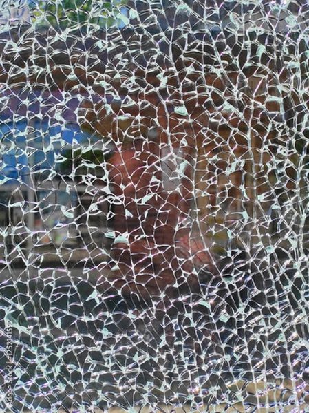Obraz A close-up view of shattered glass reveals a distorted reflection of a nearby storefront, with sunlight casting intricate patterns through the cracks
