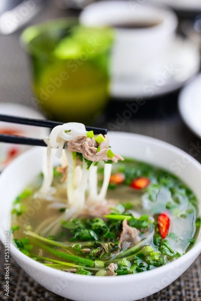 Fototapeta Chopsticks lifting noodles from beef pho