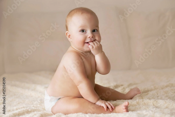 Fototapeta Cute smiling baby in a diaper on a beige couch