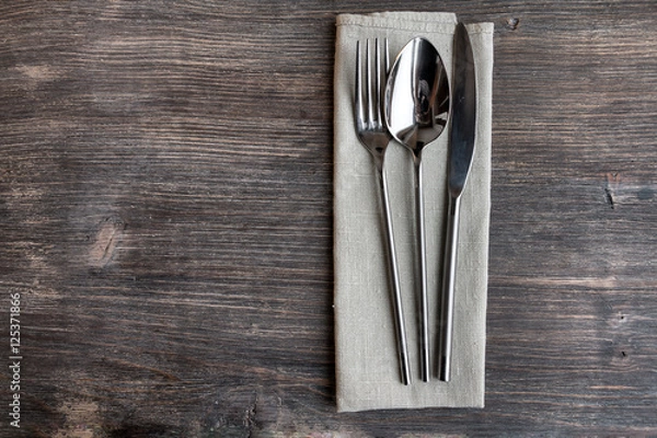 Fototapeta Concept of simple organic food - laconic design cutlery set on rustic wooden table and linen tissue. Top view.