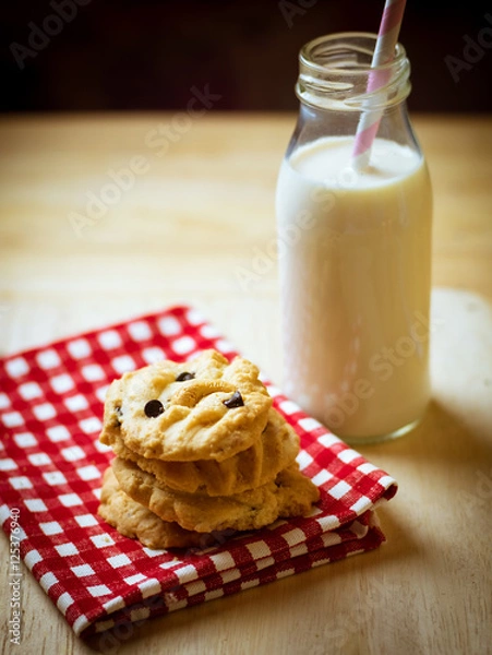 Obraz Chocolate chips and chest nut cookies on red and white checked cloth with milk and paper party straws on wood table, low key light