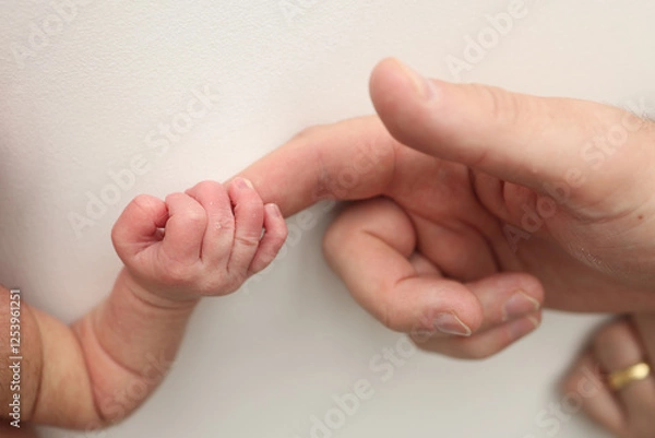 Fototapeta Close-up little hand of child and palm of mother and father. The newborn baby has a firm grip on the parent's finger after birth. A newborn holds on to mom's, dad's finger. 