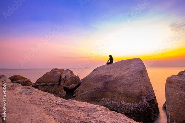 Fototapeta Man Sitting Relax On The Rocks By The Sea At Twilight Time Watching Beautiful Sky After Sunset, Long Exposure