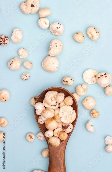Obraz Top View of Makhana or Fox Nut in a Wooden Spoon Isolated on Light Blue Background with Copy Space in Vertical Orientation, Also Known as Lotus Seed Pop, Euryale Ferox or Gorgon Nut
