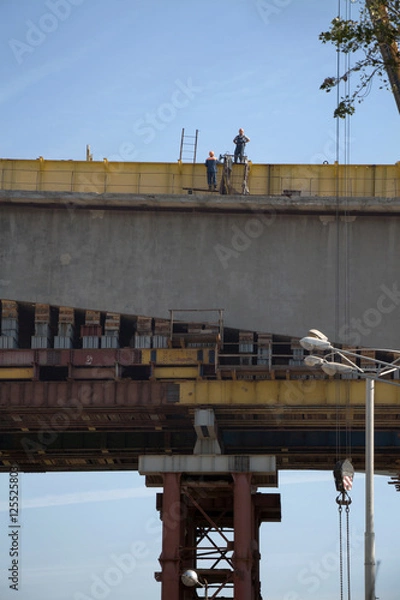 Fototapeta Two workers in workwear high on a bridge processing construction works