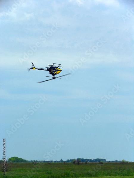 Fototapeta Model of a helicopter on the remote control flying upside down in blue sky