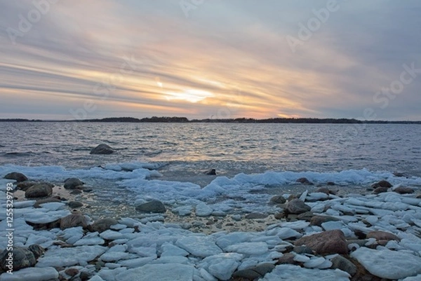 Fototapeta View of sunset from snow and ice covered rocky seashore on a cold winter day, Lauttasaari, Helsinki, Finland.