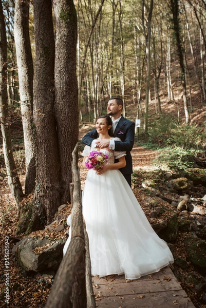 Fototapeta Portrait of beautiful bride and an elegant groom in nature, surrounded by a forest.