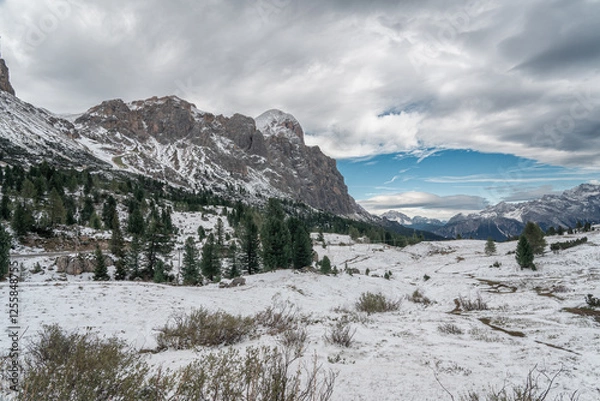 Fototapeta Snow-covered alpine meadows and towering mountains under a dynamic sky. A perfect scene showcasing the raw beauty of winter in the Dolomites.