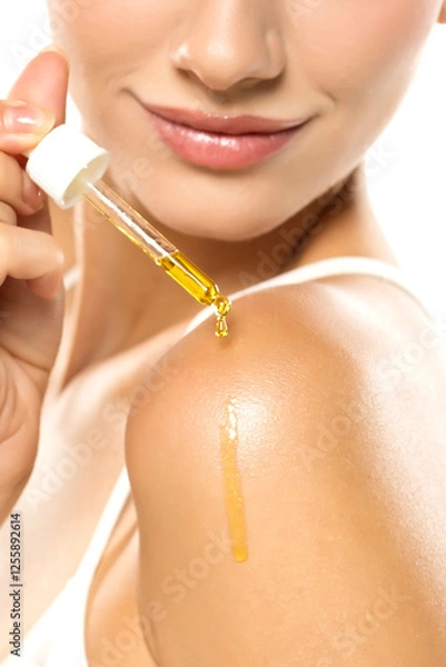 Fototapeta Golden serum droplet cascading from a pipette onto a smooth shoulder and glowing skin, with a soft, confident smile highlighting beauty and care