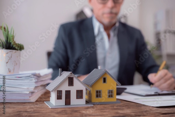 Fototapeta Miniature houses are on the wooden desk of a real estate agent calculating the investment for buying property, with documents and calculator