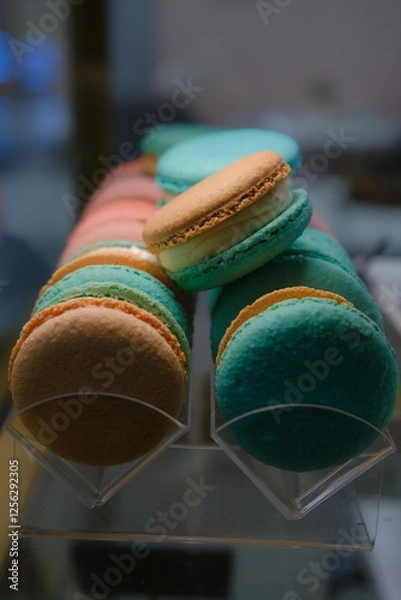 Fototapeta Close-up of colorful macarons with white cream filling displayed under soft lighting on a countertop with a blurred background and selective focus highlighting their delicate texture and vibrant hues