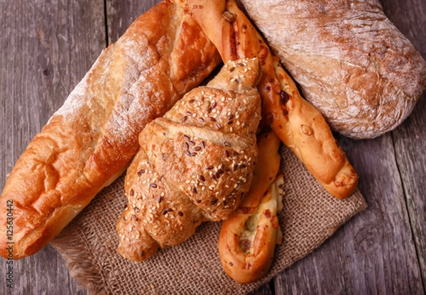 Fototapeta Assortment of fresh baked bread and croissants on burlap on rustic table