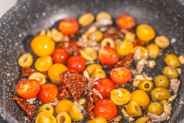 Fototapeta Cook the spaghetti Puttanesca, fry the tomatoes, anchovies, olives and capers with garlic in a pan. Close-up.