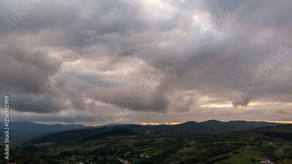 Fototapeta Majestic Mountains, Dense Forest, And Dramatic Clouds Illuminated By A Stunning Sunset. Aerial View Capturing The Breathtaking Beauty Of Nature From A Bird’s-Eye Perspective.