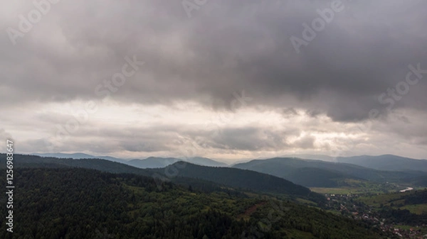 Fototapeta Magnificent Aerial View Of Mountains And Dense Forests Under Dark Clouds, With Raindrops Falling, Creating A Dramatic And Serene Atmosphere In A Remote Natural Landscape.	
