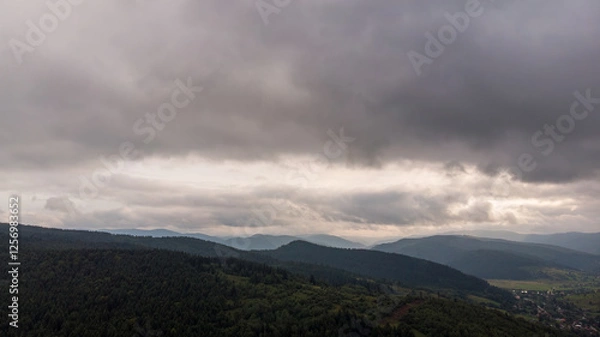 Fototapeta Majestic Mountains, Lush Green Forests, And Dramatic Clouds With The Sun Casting A Golden Glow. Aerial View Capturing The Stunning Beauty Of Nature From A Bird’s-Eye Perspective.	
