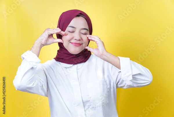 Fototapeta A joyful asian woman wearing a hijab poses playfully against a bright yellow background