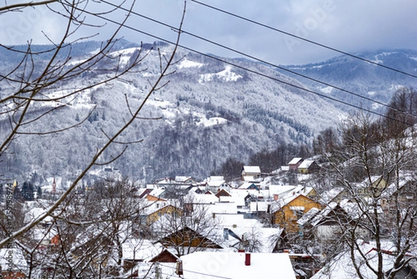 Obraz Many colorful roofs of houses in snowy mountains during winter, surrounded by snow-covered trees. A quiet countryside scene.