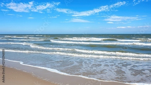 Fototapeta Serene beach scene with gentle waves lapping at the shore under a clear blue sky