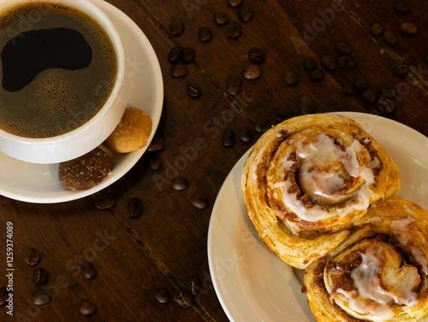 Fototapeta cup of coffee placed on a white plate with a bread on another plate, there are coffee beans scattered on the table
