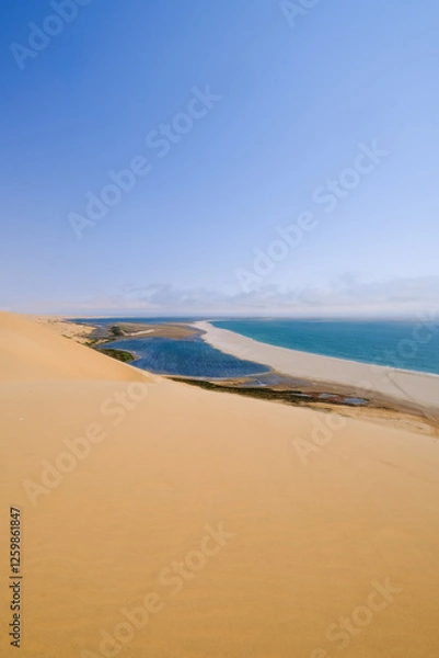 Obraz Towering golden dunes of Sandwich Harbour meet the deep blue ocean, creating a stunning contrast in Namibia's vast desert landscape.