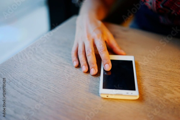 Obraz Hand Touching Smartphone on Wooden Table in Casual Indoor Setting..