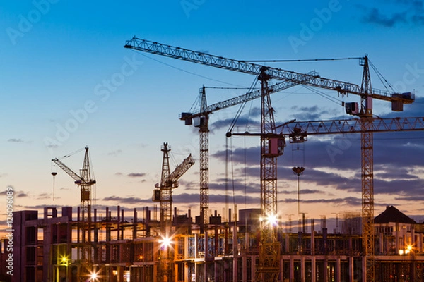 Obraz Silhouettes of tower cranes against the evening sky. House under construction. Industrial skyline