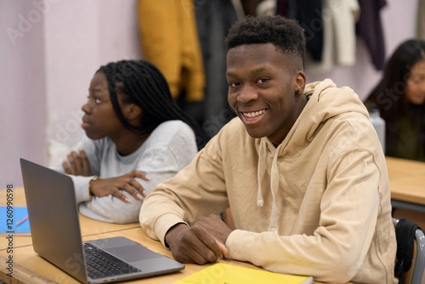 Fototapeta Smiling student using laptop in classroom with classmates attending lesson