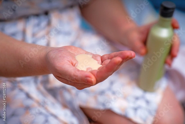 Fototapeta woman's hand holds a thick light green pine cream extracted from a plastic bottle. The creamy texture suggests nourishment and natural ingredients, ideal for skincare
