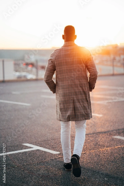 Obraz Businessman walking away at sunset in parking lot