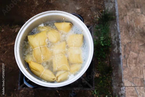 Fototapeta Photographs of a person preparing humitas using choclos, corn on the cob and a person eating humitas in a house in Chile