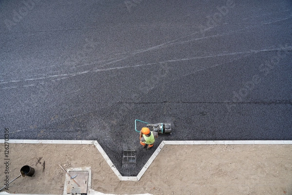 Fototapeta Aerial View of Construction Worker Finalizing Asphalt Around Drainage Grate