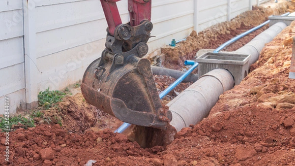 Obraz Excavator is digging soil into the drain pipe, construction of a drainage road.