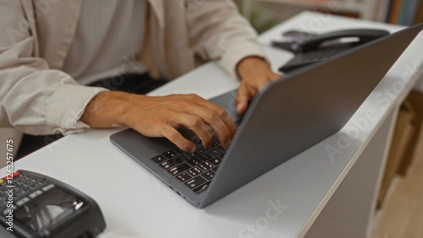 Fototapeta Young hispanic man using laptop inside a decor store
