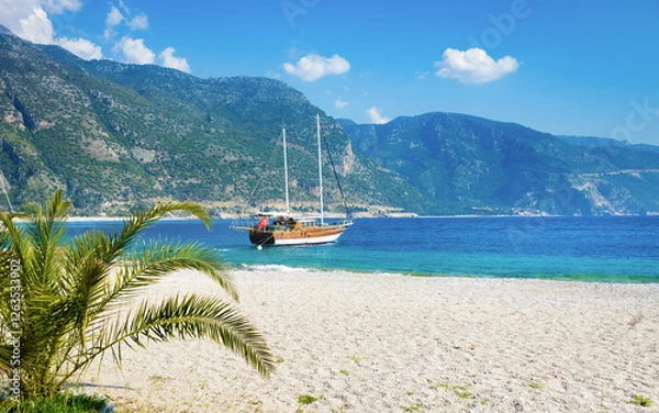 Fototapeta Oludeniz beach with blue sea, anchored sightseeing boat, majestic mountains and blue sky on Mediterranean coast of Turkey. Welcome to Oludeniz - turkish riviera