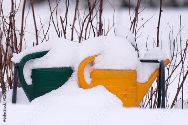 Fototapeta Green and yellow watering cans fully covered with deep snow in winter snowy scene.