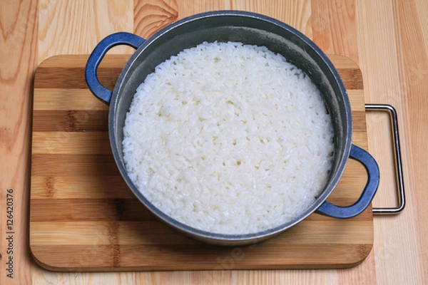 Fototapeta Boiled rice in a dark blue pan on a wooden table. Ingredients for stuffed peppers. 