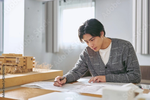 Obraz 建築の模型を横に都市計画の為の設計図を書く工学部の大学の建築学科で勉強する大学生の男性