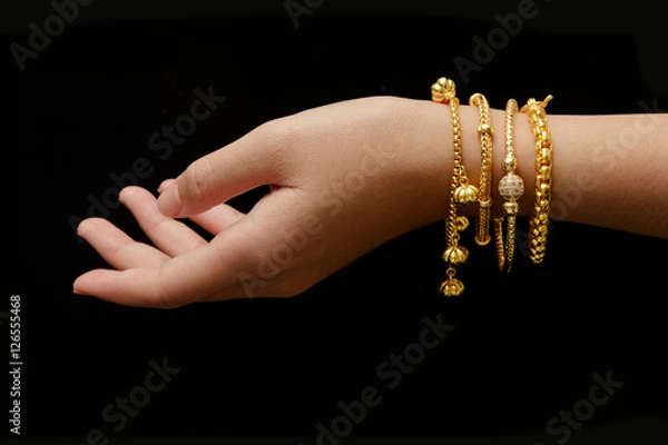 Obraz woman's hand with many different golden bracelets on black backg